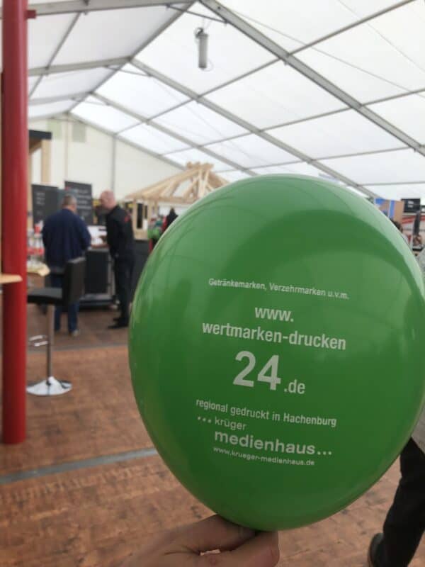 Ein hell-grüner Luftballon mit Infos zu dem Shop "wertmarken-drucken 24.de" ist zu sehen. Unter der weißen Aufschrift ist außerdem das Logo von Krüger Medienhaus, ebenfalls in weiß.